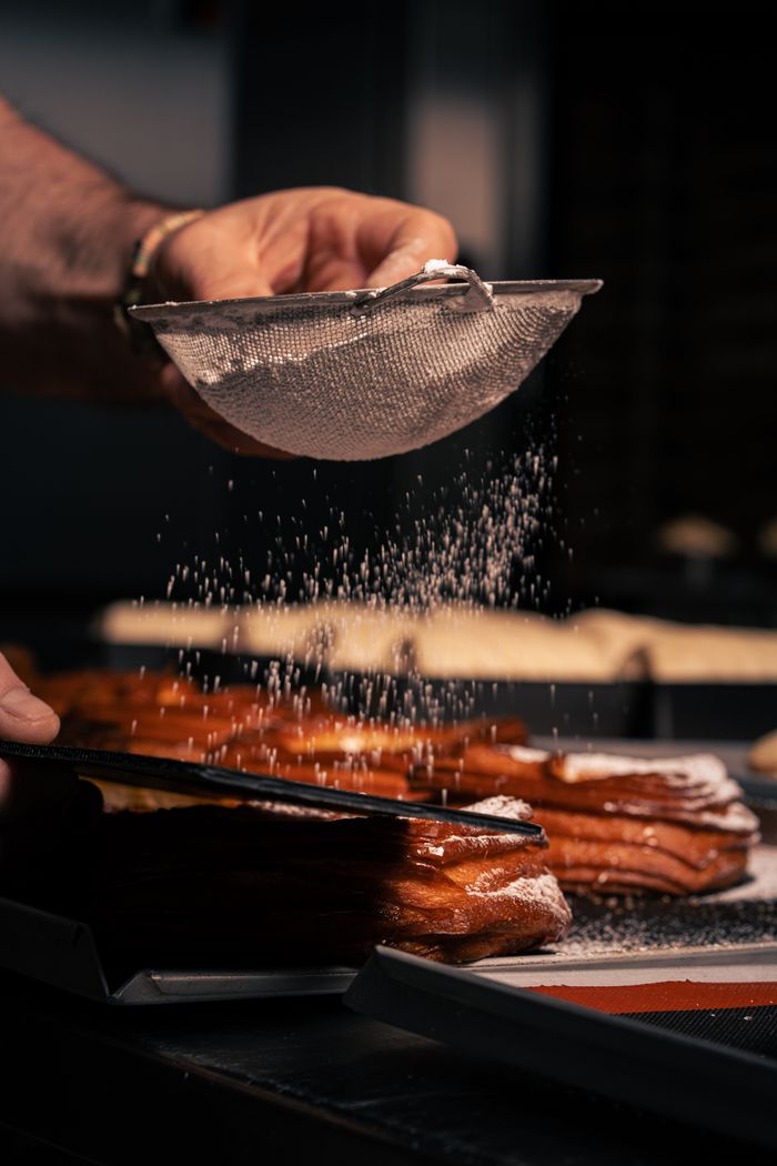 services-bg Chef carefully sprinkles powdered sugar over pastries in a professional kitchen. Perfect for culinary themes.