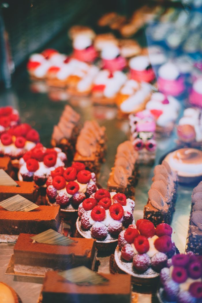 services-03 Assorted tasty cakes with chocolate and raspberry toppings placed on display behind glass in modern pastry shop with blurred background